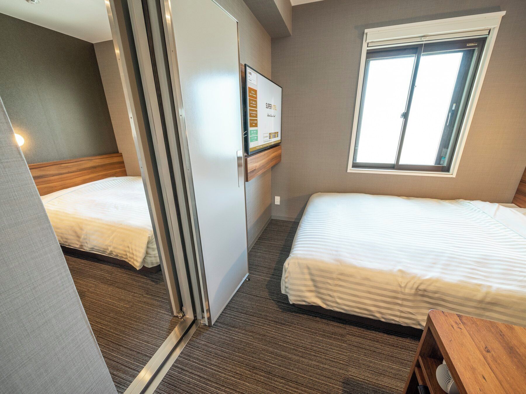 Een hotelkamer met twee bedden, een raam, een wandtelevisie en een houten bankje.