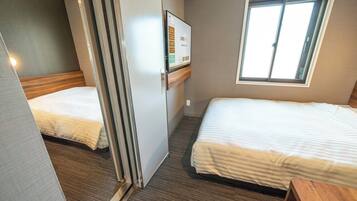 Een hotelkamer met twee bedden, een raam, een wandtelevisie en een houten bankje.