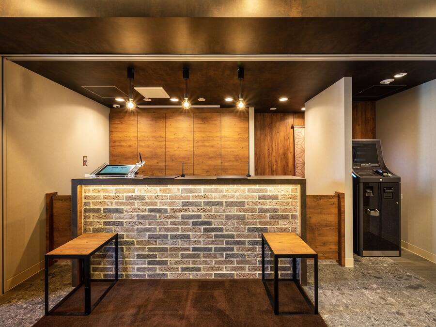 A modern kitchen with a brick backsplash, wooden cabinets, and a built-in grill. There are two stools and a laptop on the counter.