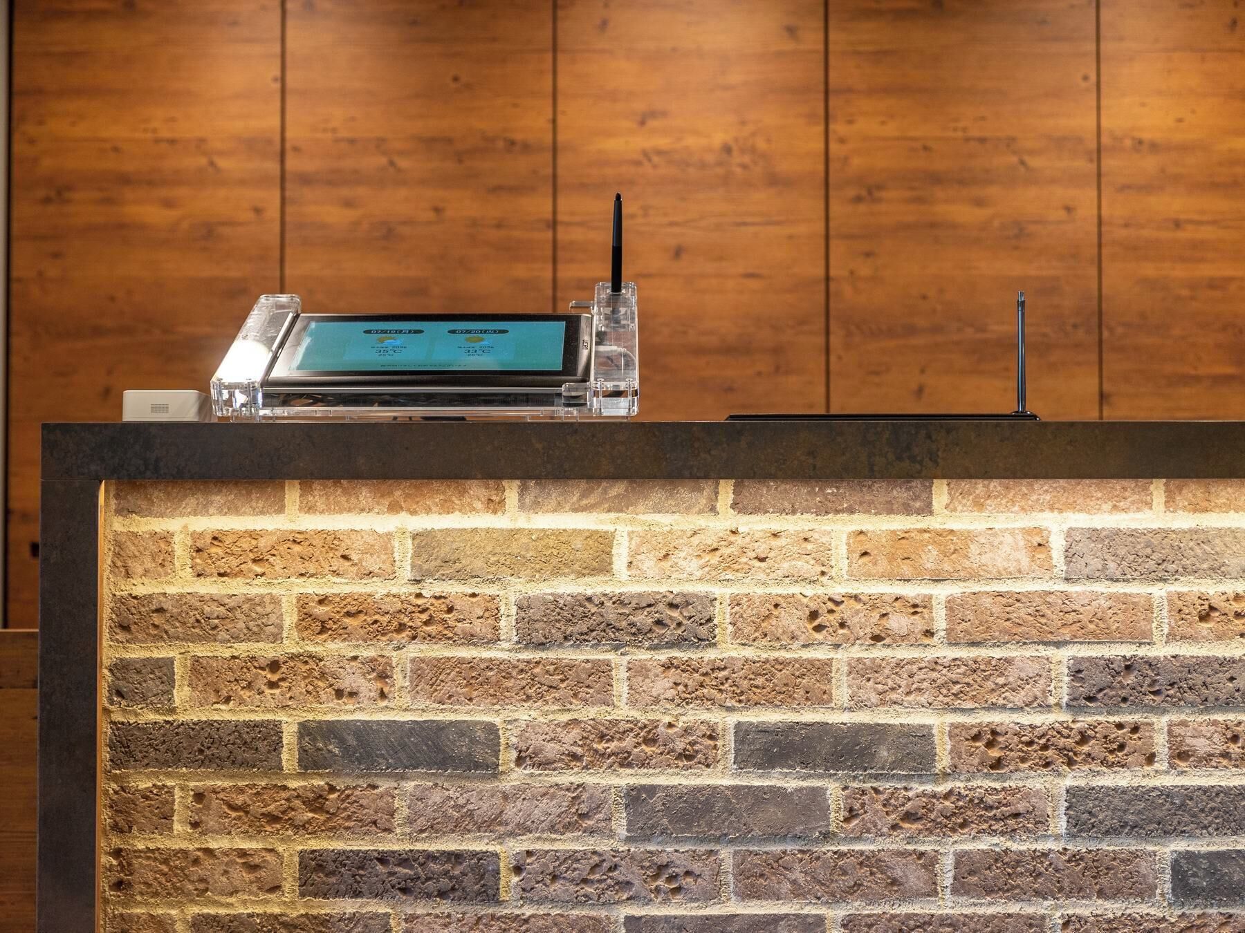Una recepción con mostrador, pantalla digital y pared de ladrillo de fondo.