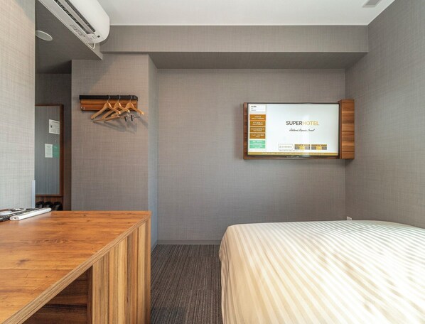 A hotel room with a bed, a desk, and a mounted screen displaying room information.