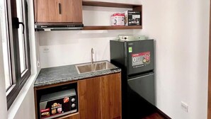 A compact kitchen with wooden cabinets, a built-in microwave, a refrigerator, and a sink. - Hoàng Huy Riverside by HPT Home (Hai Phong)