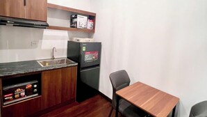 A compact kitchen with wooden cabinets, a black refrigerator, a microwave, and a small dining table with two chairs. - Hoàng Huy Riverside by HPT Home (Hai Phong)