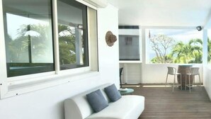 A modern room with a white sofa, a wooden deck, and a view of greenery. - Tibo villa bottom Access 4 beaches in Deshaies (Deshaies)