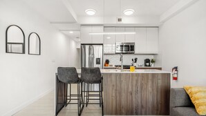 A modern kitchen with a central island, two bar stools, and a grey sofa. - Modern Ground-Level Suite UG Parking, AC, C-Train (Calgary)