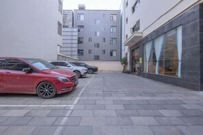 A parking area with multiple cars, a building with large windows, and a paved walkway. - Junlong Hotel (Jianshui)