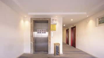 A hallway with an elevator, a framed notice, and a door at the end.
