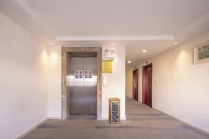 Un pasillo con un ascensor, un anuncio enmarcado y una puerta al final.