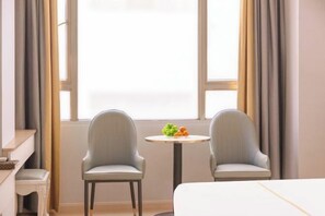 A hotel room with two armchairs, a small round table with fruit, and a bed. - Junlong Hotel (Jianshui)