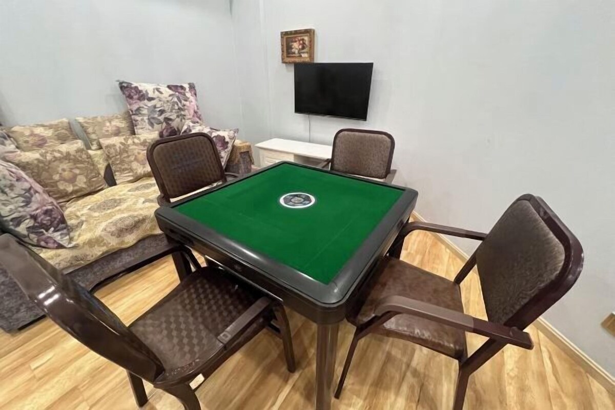 A room with a pool table, four chairs, a sofa with floral cushions, a flat-screen TV, and a small table.
