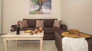 A living room with a brown sofa, a wooden coffee table with a wine bottle, glasses, and decorative items.