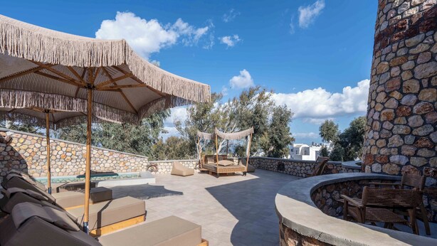 A rooftop terrace with lounge chairs, a stone wall, and a pergola with a canopy.