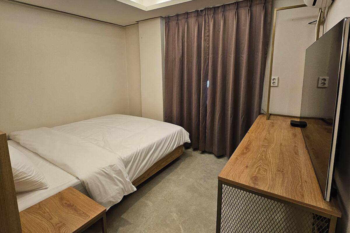Une chambre d’hôtel avec un lit simple, un bureau en bois, une télévision et une fenêtre avec des rideaux.