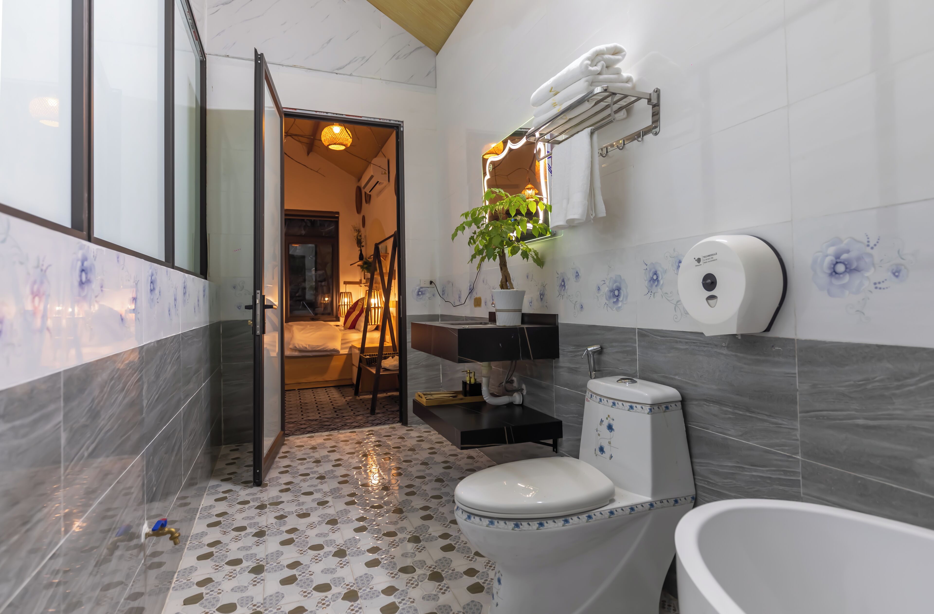 A modern bathroom with a toilet, sink, and bathtub. There is a potted plant on the sink counter and a towel rack above the mirror.