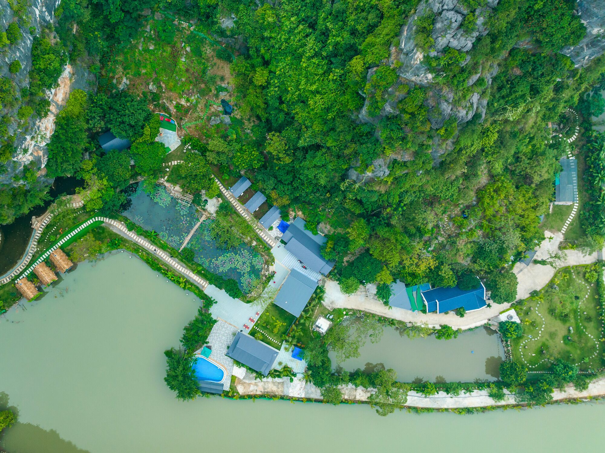 Vista aérea de un resort con piscina, varias construcciones y un paisaje natural circundante.