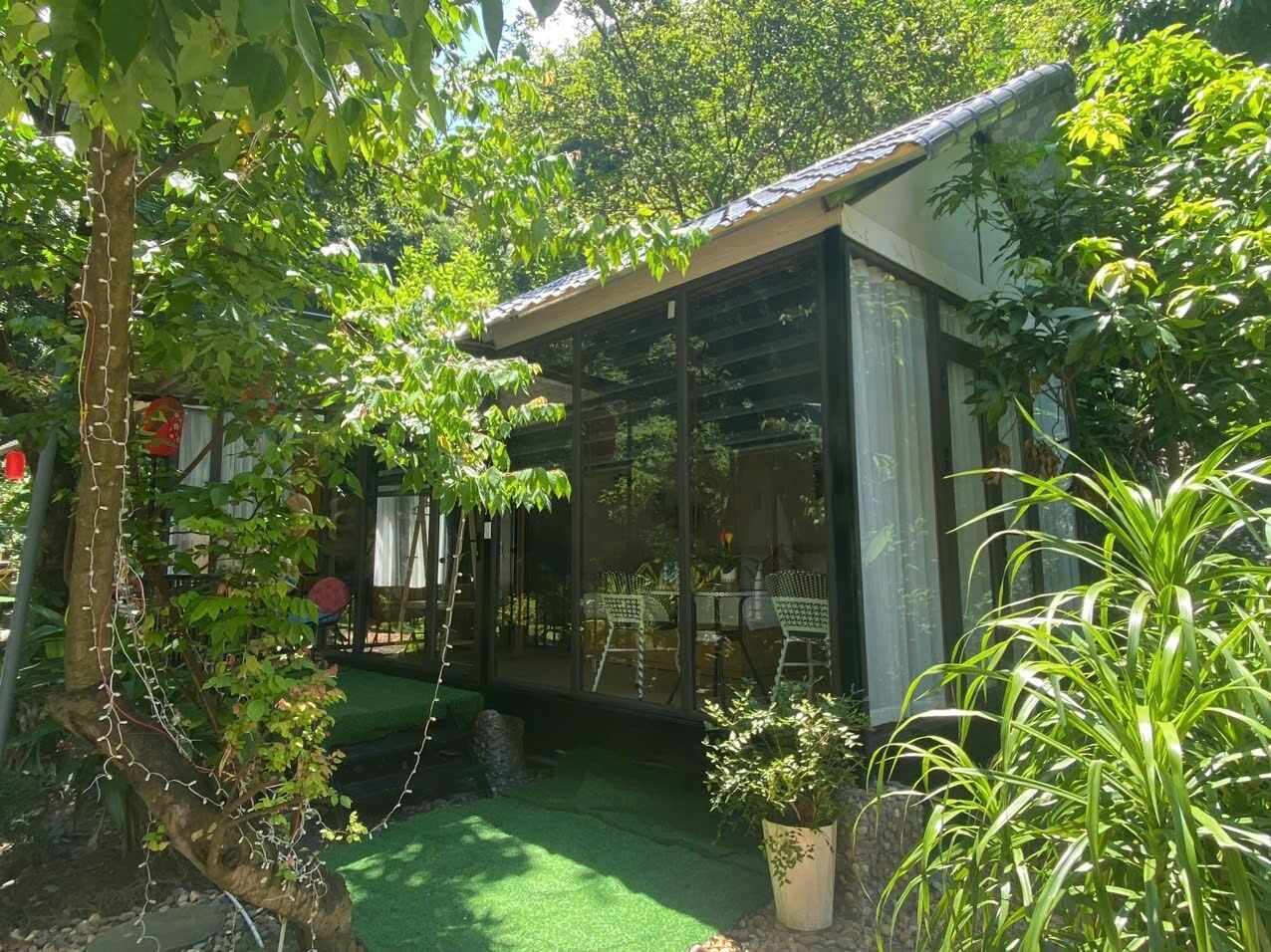 Un espacio de estar al aire libre cubierto con cerramiento de vidrio, rodeado de abundante vegetación y un pequeño jardín.