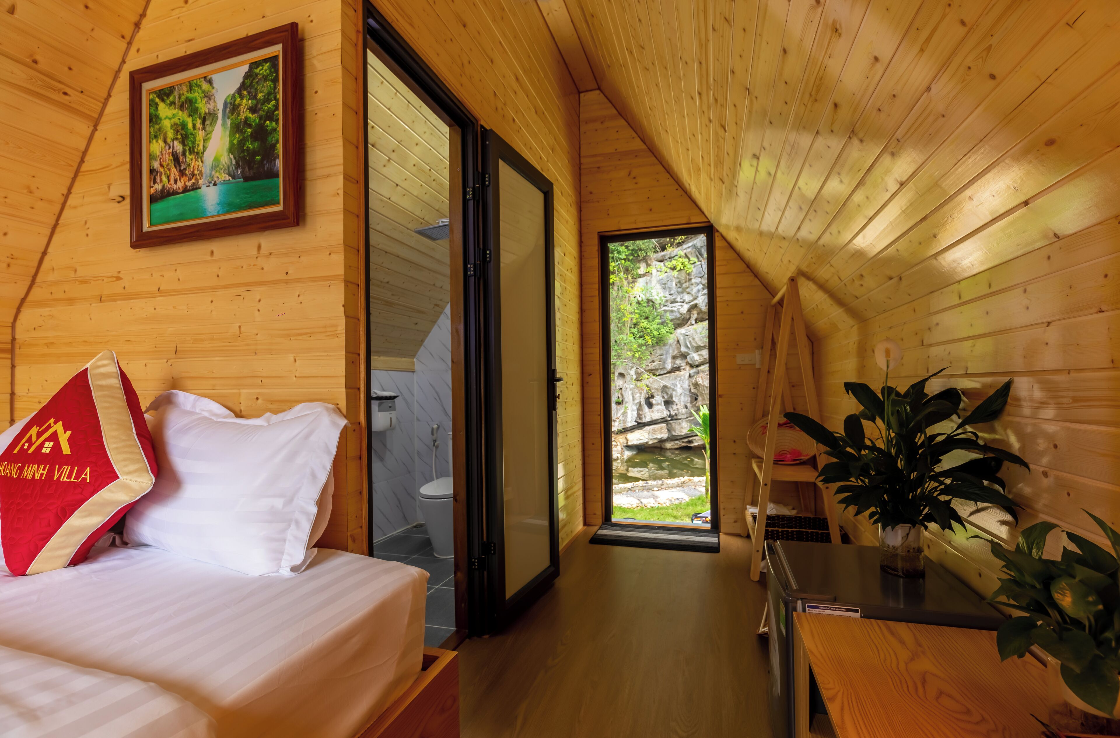 A wooden cabin interior with a bed, a bathroom, and a view of a rocky landscape.