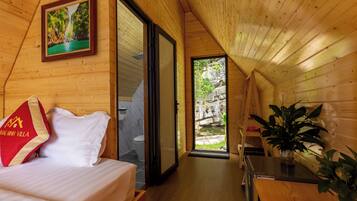 Interior de una cabaña de madera con cama, baño y vista a un paisaje rocoso.