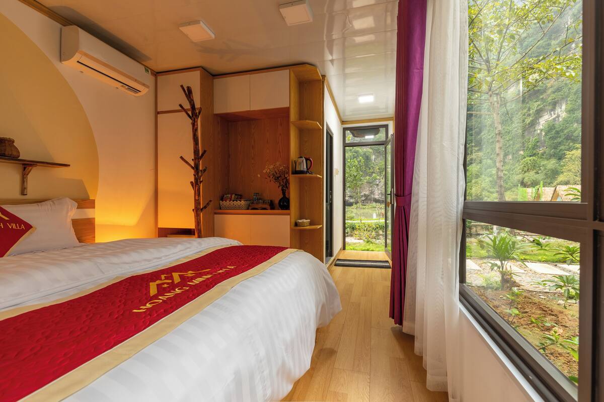 Une chambre d’hôtel avec un grand lit, une armoire en bois, un bureau et une vue sur un jardin luxuriant.