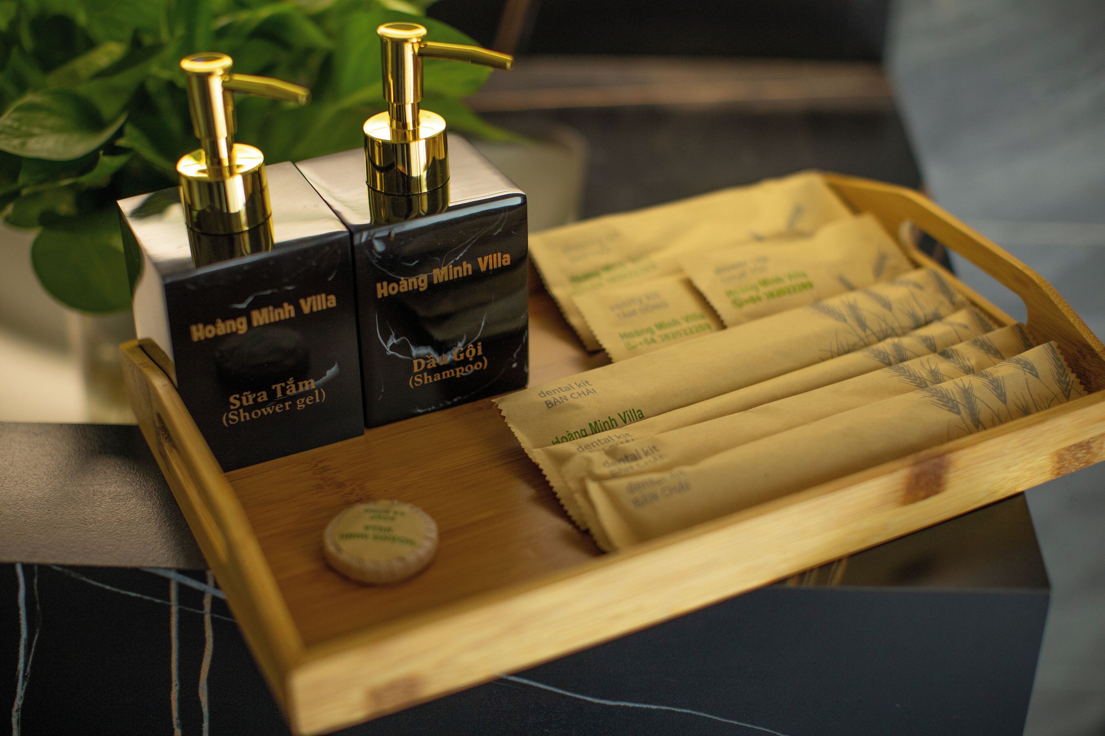 A tray with two black boxes labeled 'Hoàng Minh Villa' and 'Shampoo,' a wooden tray, and several packaged items.