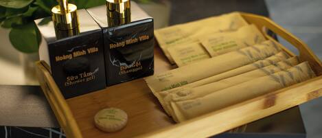 A tray with two black boxes labeled 'Hoàng Minh Villa' and 'Shampoo,' a wooden tray, and several packaged items.