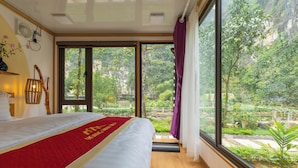 Un dormitorio con una cama grande, un corredor rojo y vistas a un jardín exuberante a través de una puerta corrediza.