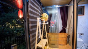 Una habitación con una bañera de madera, un estante de madera y vistas al exterior.