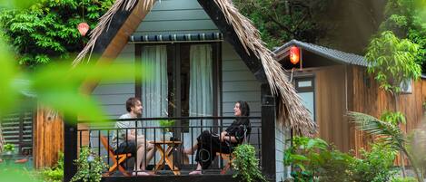 A house with a thatched roof, a porch with two chairs, and a small table.