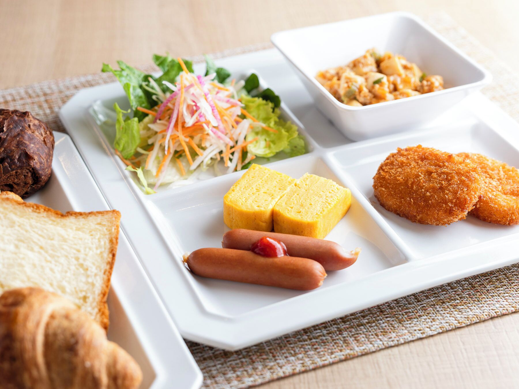 Una bandeja con diversos alimentos, incluyendo pan, perritos calientes, frituras y una ensalada.