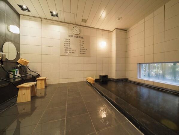 Un onsen japonés tradicional con un banco de madera, un espejo y un reloj en la pared.