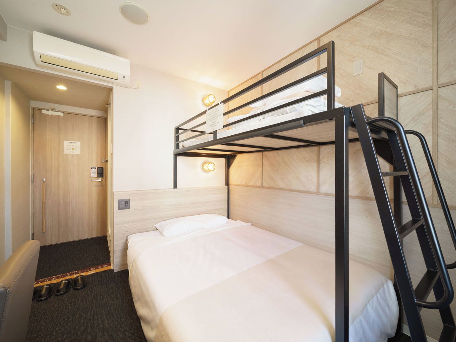A bunk bed room with a wooden door, a shoe rack, and a wall-mounted light fixture.