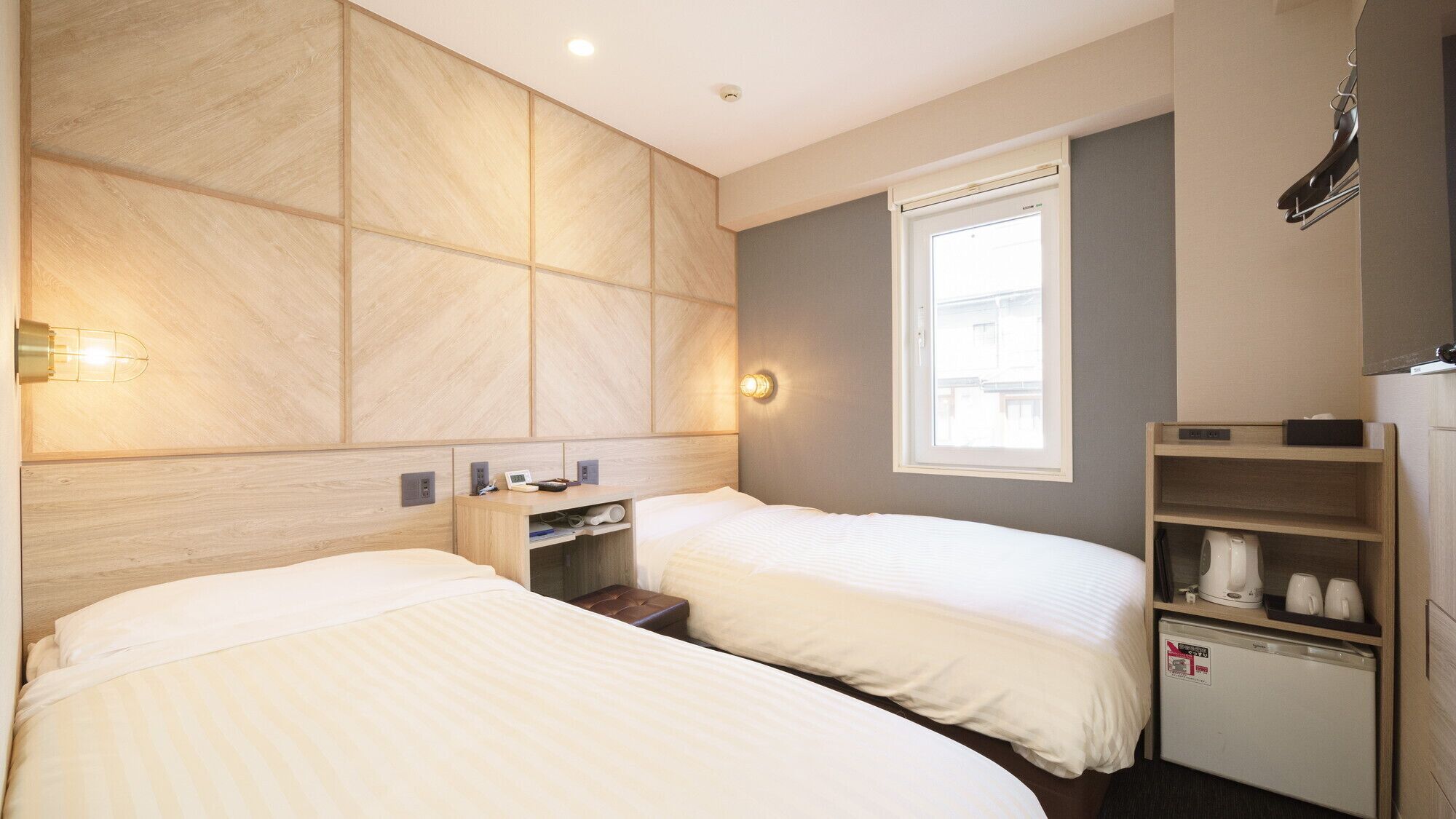 A hotel room with two beds, a small desk, a mini-fridge, and a window with a view.
