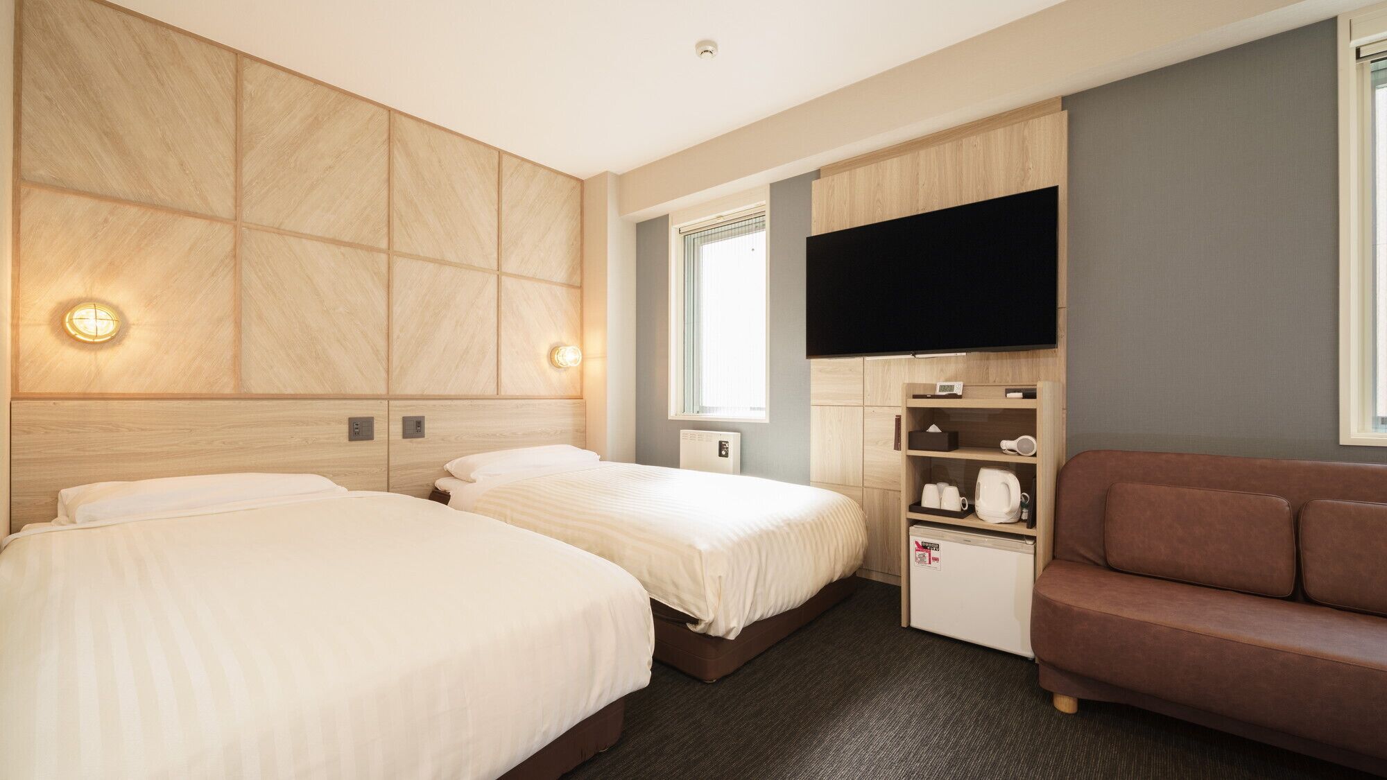 A hotel room with two beds, a television, a small kitchenette, and a sofa.