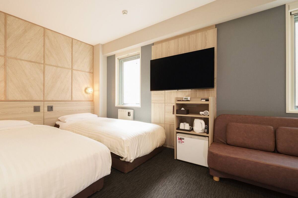 A hotel room with two beds, a television, a small kitchenette, and a sofa.