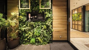Una zona de recepción con pared de madera, follaje verde y un panel informativo digital.