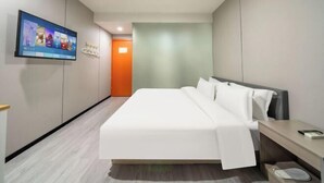 Una camera d'albergo moderna con un letto, una TV fissata al muro e un corridoio che porta a una porta arancione.