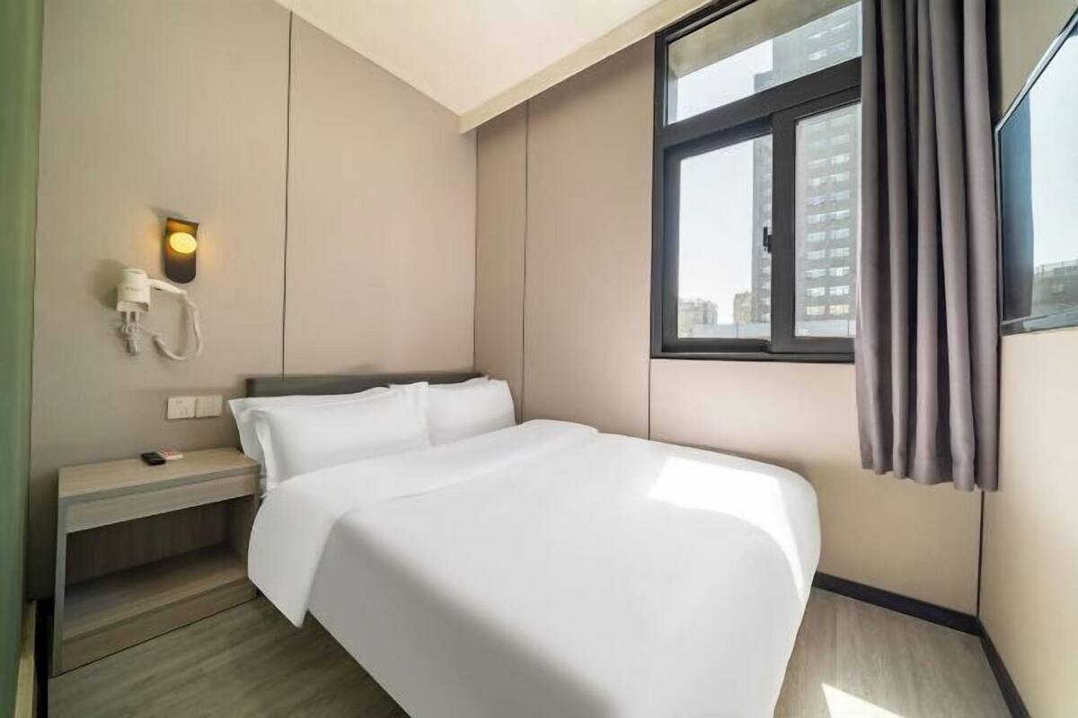 Ein Hotelzimmer mit Bett, Nachttisch, Lampe und einem Vorhangfenster.