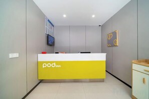 A reception desk with a yellow and white color scheme, a television mounted on the wall, and a framed artwork above it. - Pod Choice Hotel (Hangzhou Huanglong Sports Centre Wensan Road Subway Station) (Hangzhou)