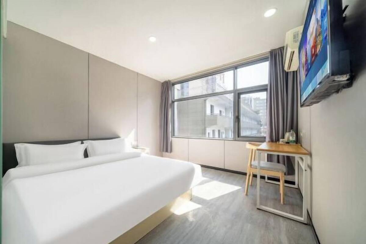 Ein Hotelzimmer mit einem großen Bett, einem Schreibtisch, einem Sessel, einem Fernseher und einem Fenster mit Vorhängen.