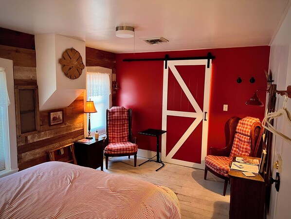 A room with a bed, two chairs, a lamp, a window with curtains, a wall clock, and a red door. - 3-bedroom FarmHouse with WiFi, Large Gathering Room, Dining kitchen in Nappanee (Nappanee)
