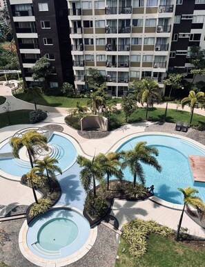 A multi-level residential building with balconies, a landscaped pool area with palm trees, and a small garden. - K2 Nordic-inspired Cozy Space (Iloilo)