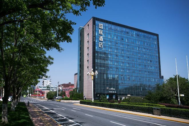 A modern hotel building with a glass facade and a clear blue sky in the background.
