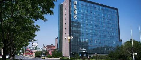 A modern hotel building with a glass facade and a clear blue sky in the background.