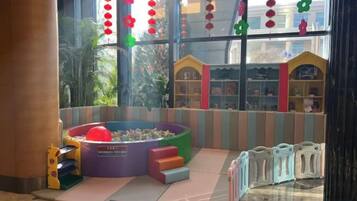 Zona de juegos infantiles con piscina de pelotas, estructuras de juegos blandos y vista a un edificio con fachada colorida.