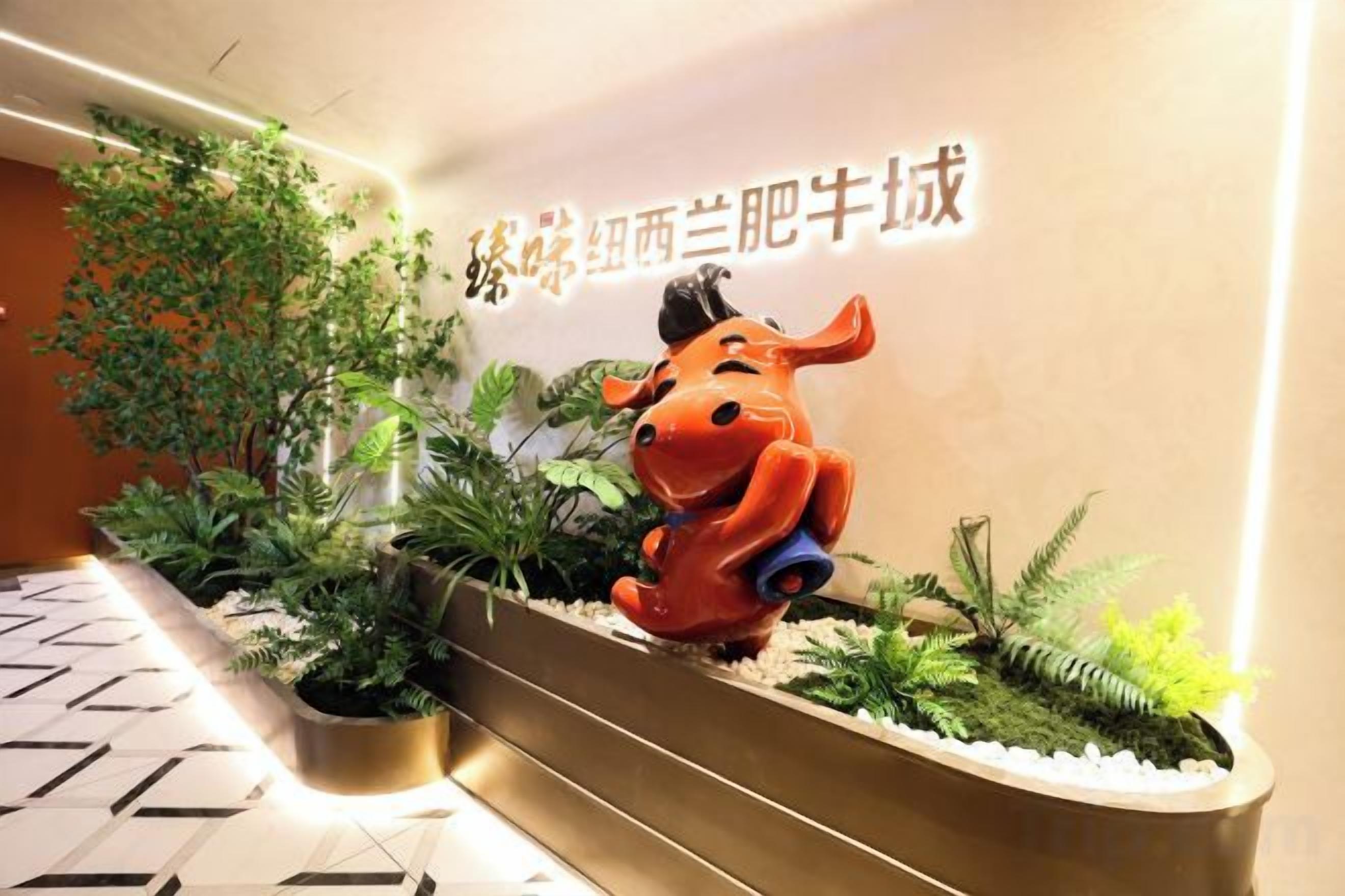 Un espace d’accueil agrémenté d’une sculpture représentant un animal, de plantes d’intérieur et d’un mur orné de texte.