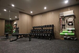 Un gimnasio con equipo de levantamiento de pesas, una banca y un rack de pared con varios objetos.