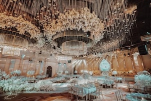 Un amplio salón con varias mesas y sillas, candelabros ornamentales y un gran arco decorativo.