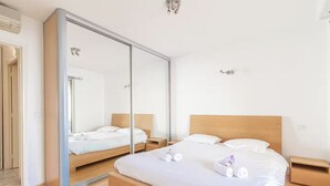 A modern bedroom with a large bed, a wardrobe, and a mirror.