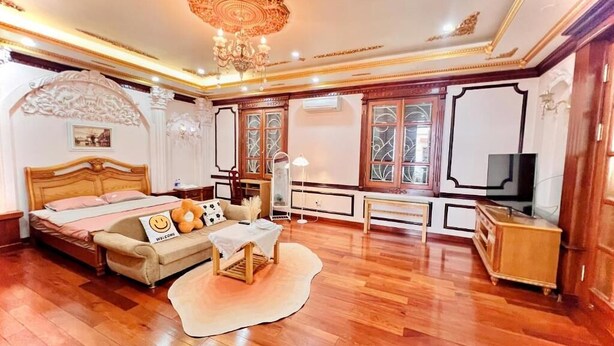 Une chambre spacieuse avec un grand lit, une commode en bois, un téléviseur et un lustre.