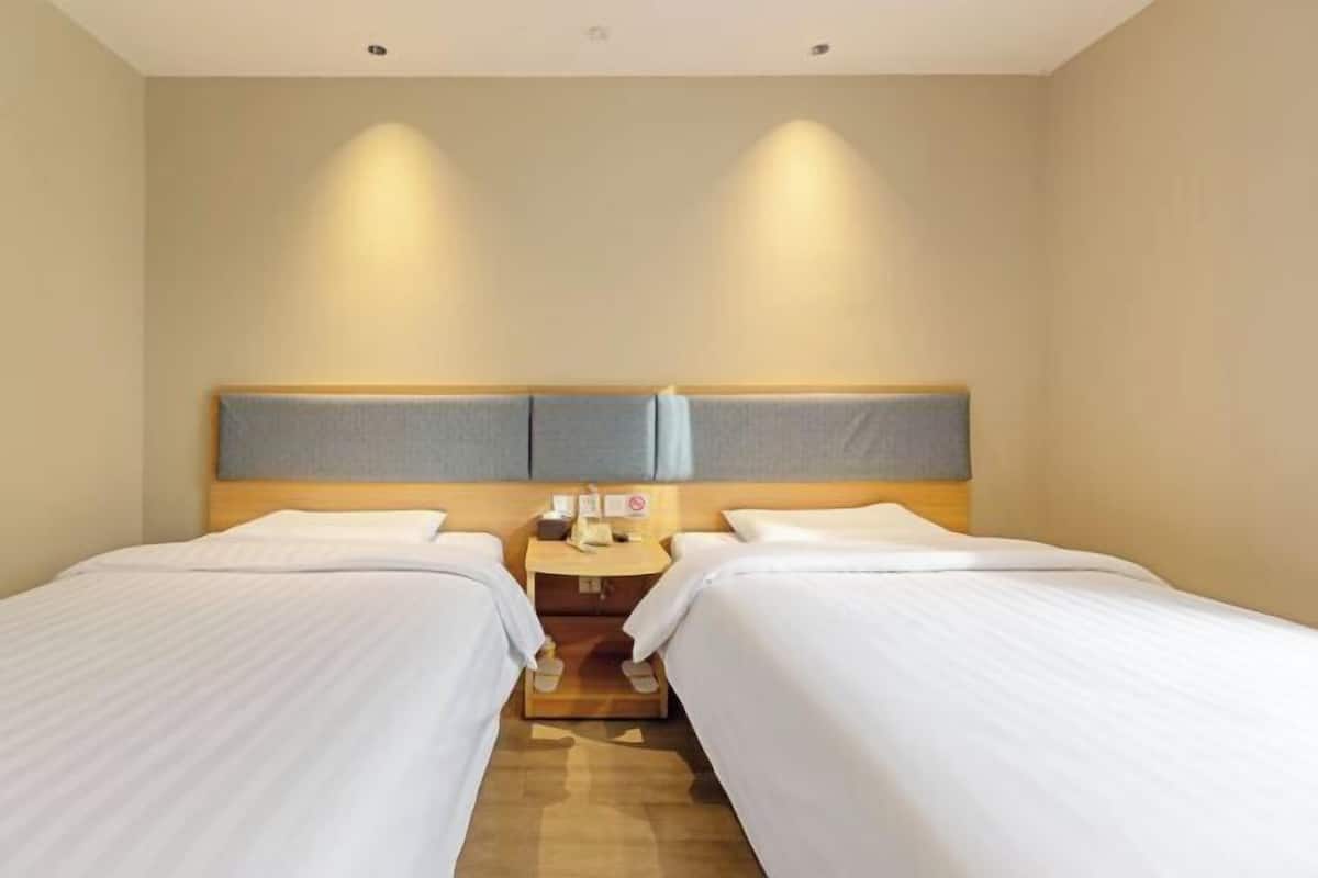 A hotel room with two beds, a wooden nightstand, and a headboard with built-in lighting.